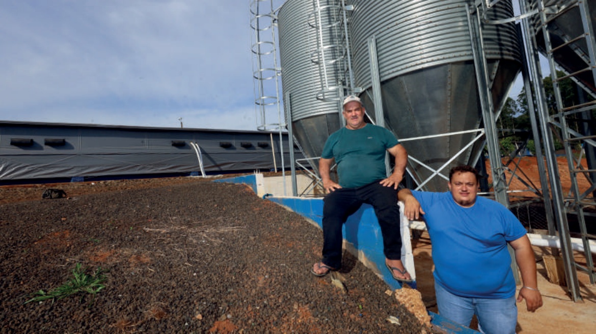 Cooperados em Ipua&ccedil;u, Adir e Luiz Fernando Spada, em frente a um avi&aacute;rio e silos de armazenamento.