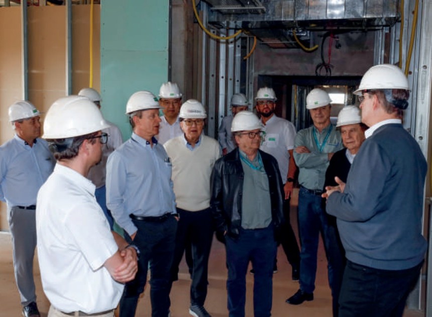 Diretores com capacetes de seguran&ccedil;a dentro da obra do hospital, ouvindo explica&ccedil;&otilde;es.