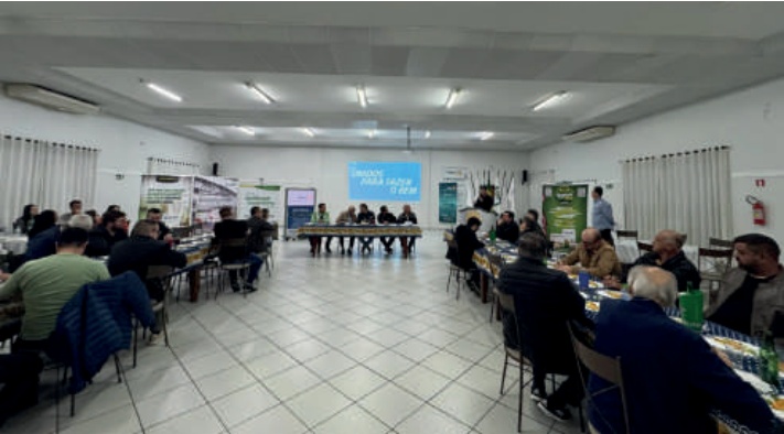 Vis&atilde;o geral de uma sala com pessoas sentadas em mesas durante um evento de formatura.