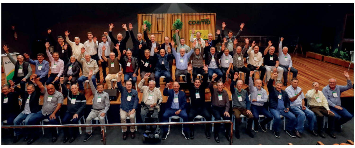 Foto em grupo dos gestores participantes do encontro, sentados em um palco e acenando.