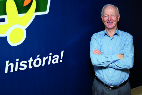 Guntolf van Kaick sorrindo com os bra&ccedil;os cruzados em frente a um painel azul com a palavra 