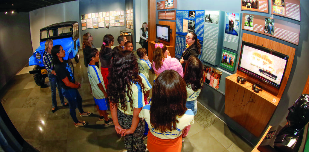 Visitantes, incluindo um grupo de estudantes, observam as exposi&ccedil;&otilde;es no Memorial Coamo.
