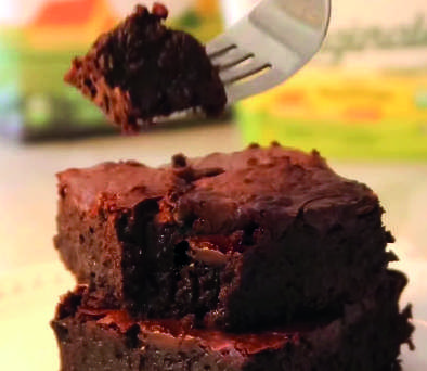 Um peda&ccedil;o de brownie em um garfo, com mais brownies ao fundo.