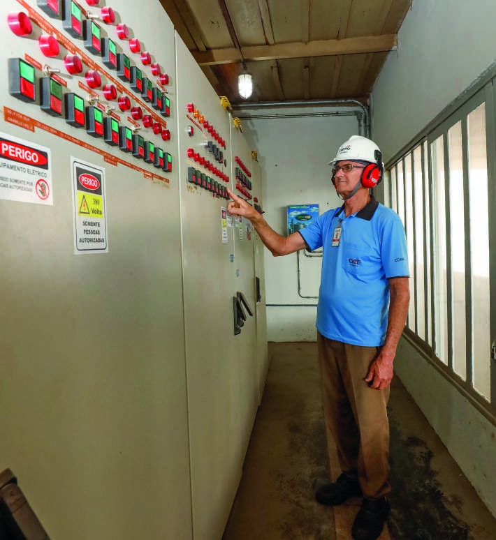Funcion&aacute;rio da Coamo, de capacete e protetor auricular, opera um grande painel el&eacute;trico industrial.